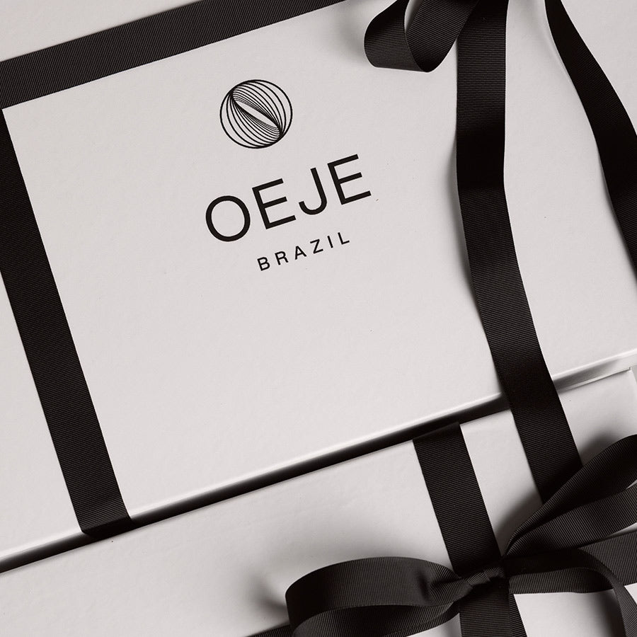 Duas caixas de presente brancas OEJE BRAZIL, amarradas com fitas pretas, uma com laço.